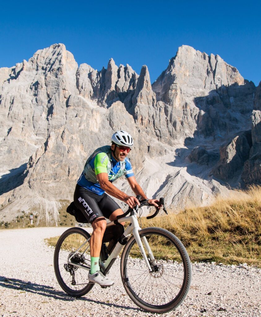 A gravel rider with bikepacking bags rides under pale Dolomite rock towers