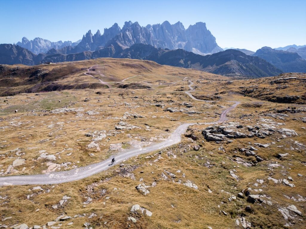 A high plateau of golden pastures crossed by a gravel road, Dolomite spires on the horizon