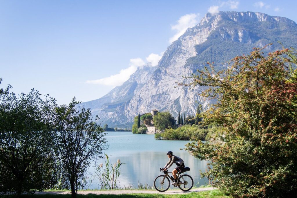 A rider passes a lake with a castle on the water and a rock wall behind