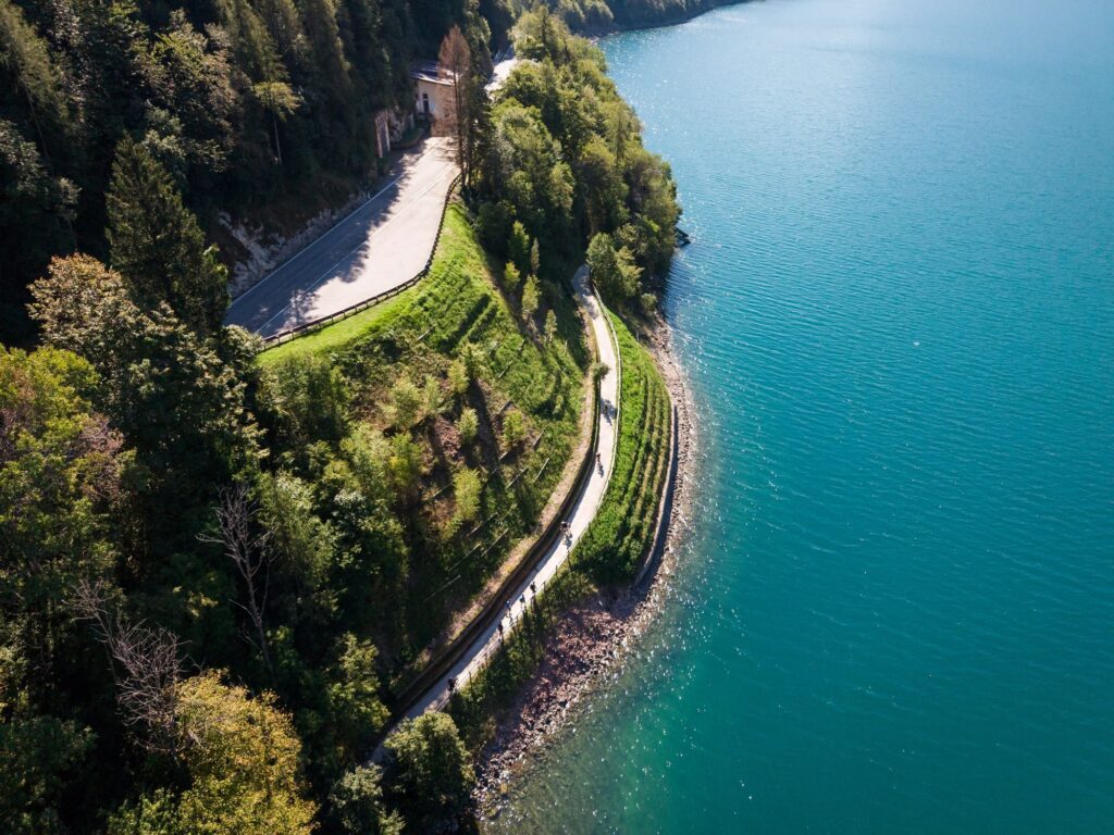 From above, a forest road runs along a turquoise lake