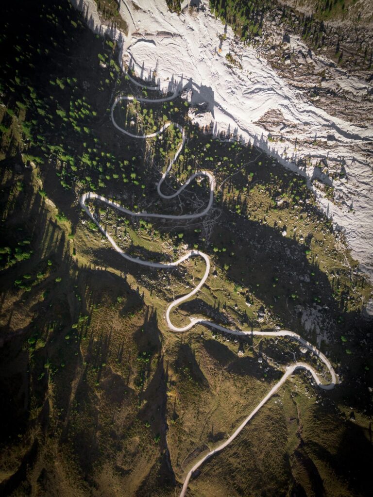 From above, gravel switchbacks climb through the forest under a rock wall