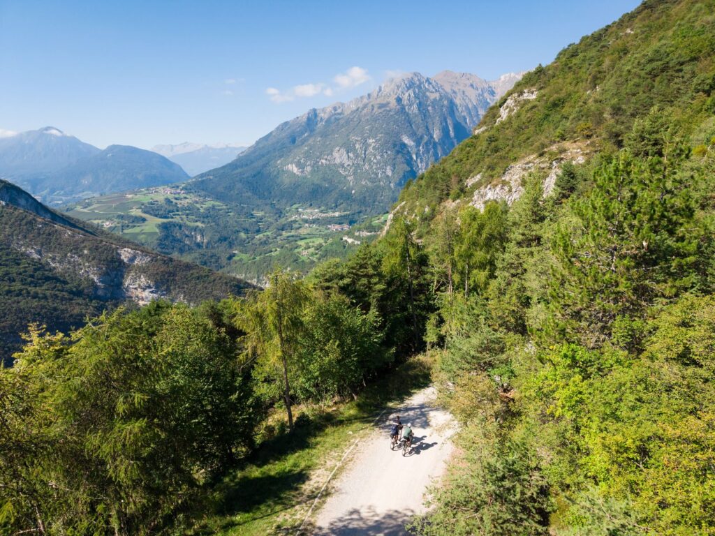From above, a gravel road runs through a green valley toward the mountains