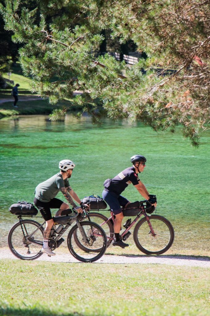 Two gravel riders side by side along an emerald green lake