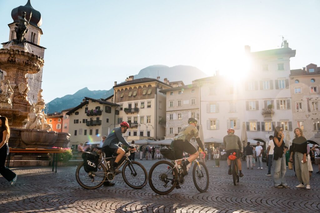 Riders with bikepacking bags cross Piazza Duomo in Trento next to the Neptune fountain