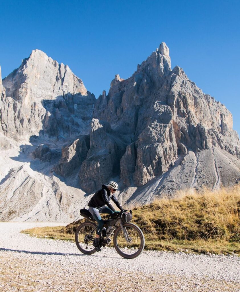 A rider on gravel under the jagged peaks of the Pale di San Martino