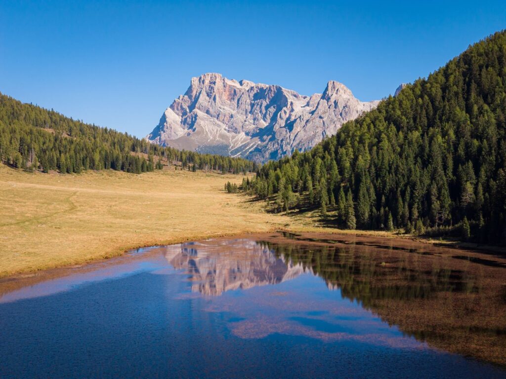 A mountain lake reflects a Dolomite peak between forests