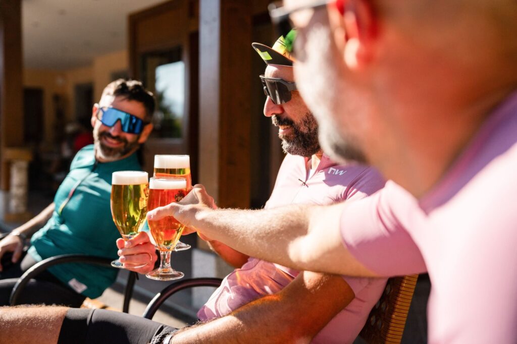 Three riders raise glasses of beer at a bar table, smiling