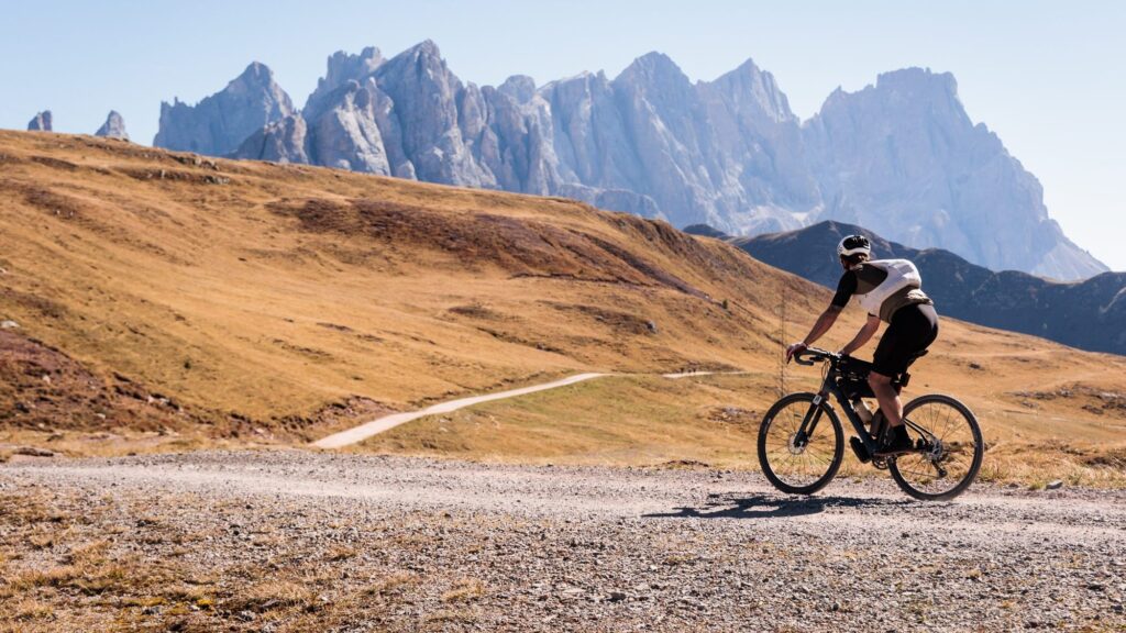 A lone rider on a gravel road across a high plateau under the peaks