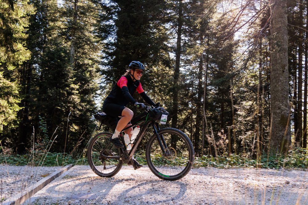 A rider with bikepacking bags rides through a pine forest