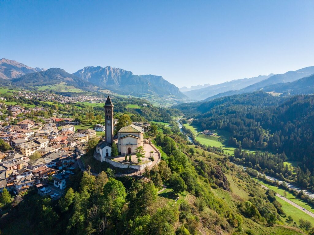 A village with a bell tower on a hill above a green valley, mountains behind